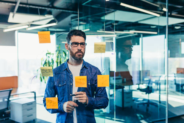 istock focused and thinking businessman writing on colorful notes attached to a glass wall, the entrepreneur creates a visual to-do list, business goals for future careers, daily goals, the concept of completed tasks 1365402421