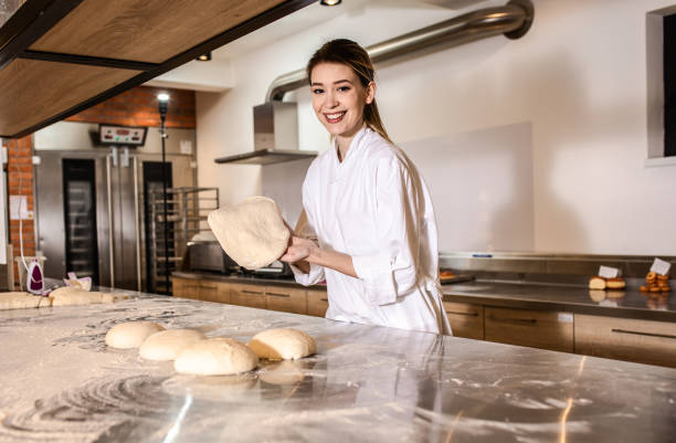 istock Young female baker preparing dough for bread in modern manufacturing. 1365402787