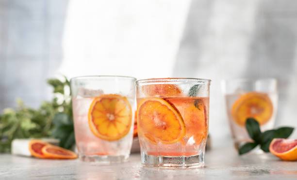 istock Cold refreshing drink with tonic, blood Sicilian oranges and ice, grey concrete background. Cocktail with tonic and oranges. Direct sunlight and hard shadows. 1365404508