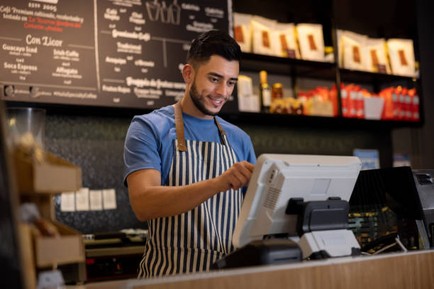 Happy man working as a cashier at a cafe Portrait of a happy Latin American man working as a cashier at a cafe and placing an order in the computer cashier stock pictures, royalty-free photos & images