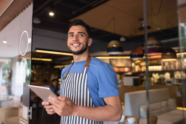 istock Waiter working at a cafe waiting for clients at the door 1365404983