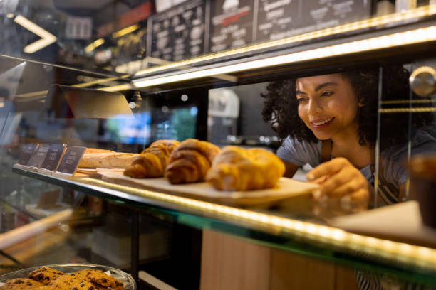 Happy waitress working at a cafe and placing pastries in the counter display