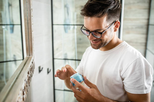 istock Young man going through morning routine in the bathroom applying face cream. 1365406349