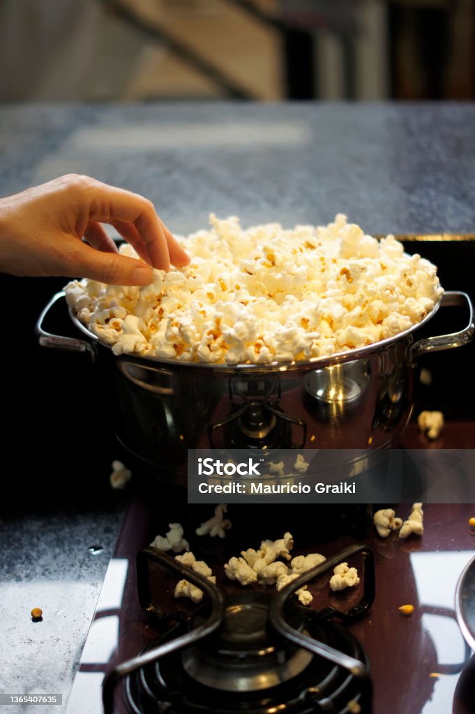 A stainless pan full of popcorn. Focus on the edge of the pan. Soft focus background Popcorn Stock Photo