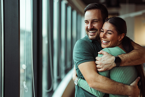 Happy caucasian partners, looking through the window of their hotel room.