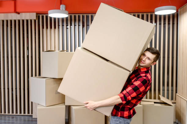 istock Young man, a courier, is carrying a cardboard box in a post office store. 1365409041