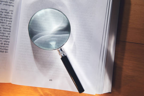 istock Magnifying glass and open books on wood table. 1365410382