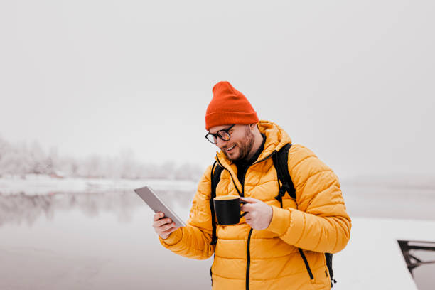 istock Man drinking hot drink and using phone in winter snowy day 1365411042