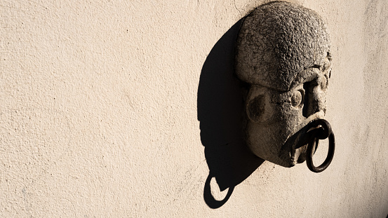 detail of statue with horse hook on the wall. depiction of a stylized face, antique style.
