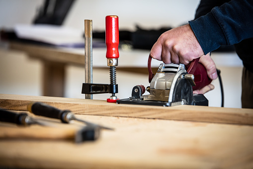 carpenter or craftsman cuts wood with an electric circular saw in a workshop