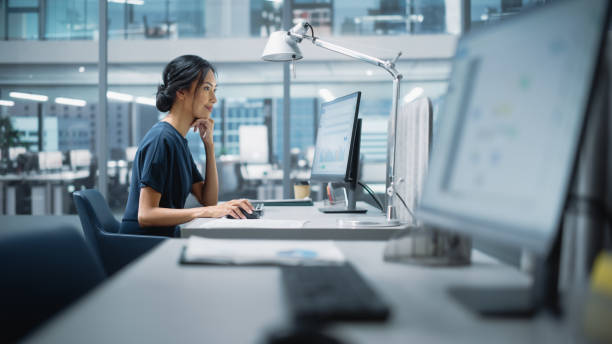 dans un grand bureau d’entreprise diversifié: portrait d’un beau gestionnaire asiatique utilisant un ordinateur de bureau, femme d’affaires gérant les opérations de l’entreprise, analysant les statistiques, les données commerciales, les plans m - technologie financière photos et images de collection