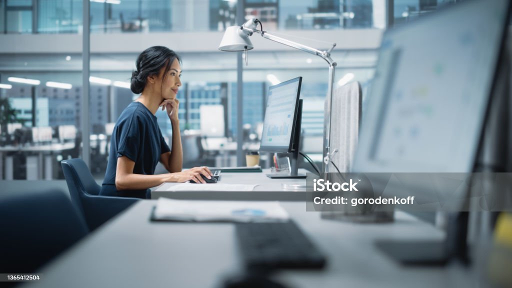 In Big Diverse Corporate Office: Portrait of Beautiful Asian Manager Using Desktop Computer, Businesswoman Managing Company Operations, Analysing Statistics, Commerce Data, Marketing Plans. Office Stock Photo