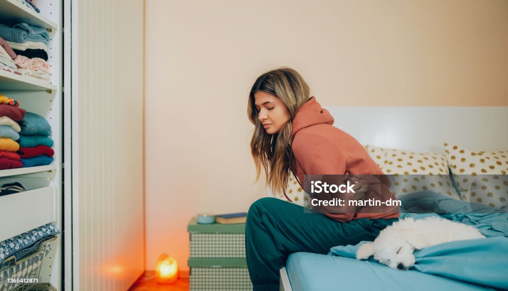 Woman with stomach pain staying home Young woman with painful menstruation resting in bed Menstruation Stock Photo