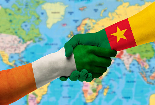 Handshake between Cameroon and CÃ´te d'Ivoire flags painted on hands.With background of world map