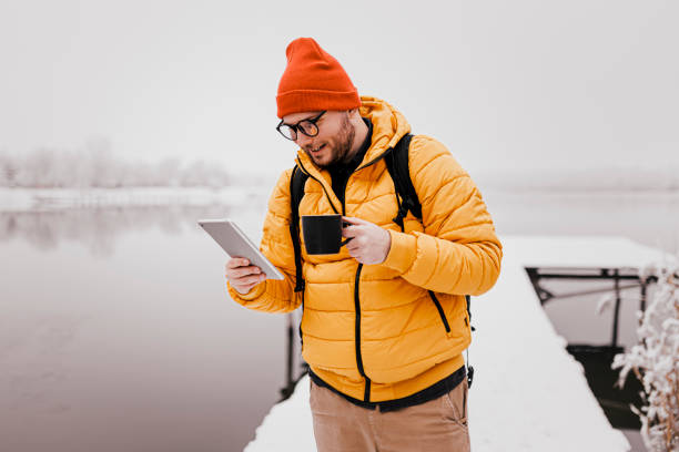 istock Man drinking hot drink and using phone in winter snowy day 1365413958