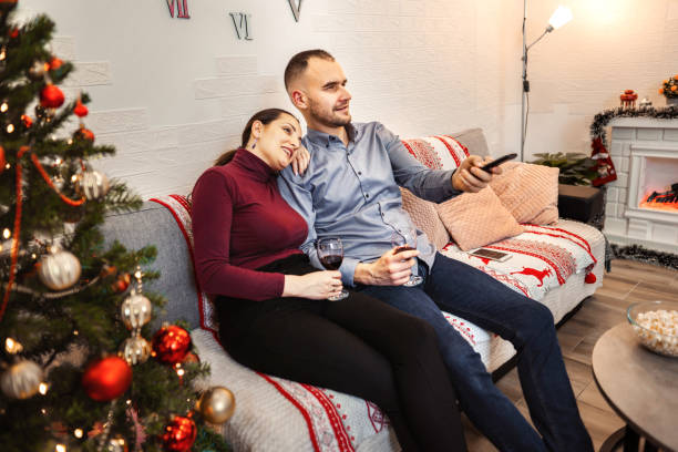 istock Young happy couple watching television and drinking wine during Christmas 1365414019