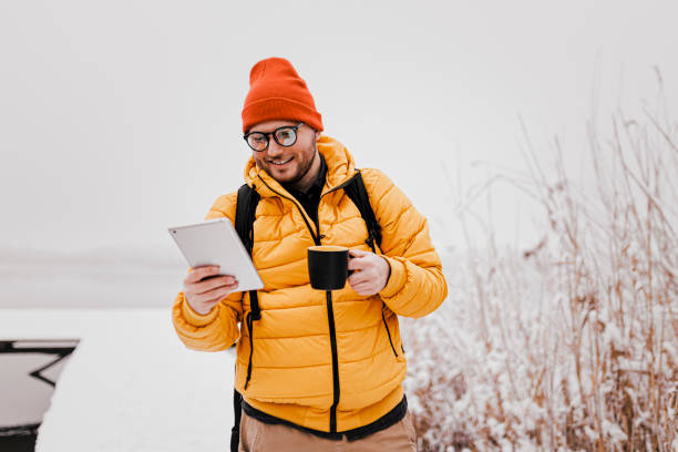 istock Man drinking hot drink and using phone in winter snowy day 1365414480