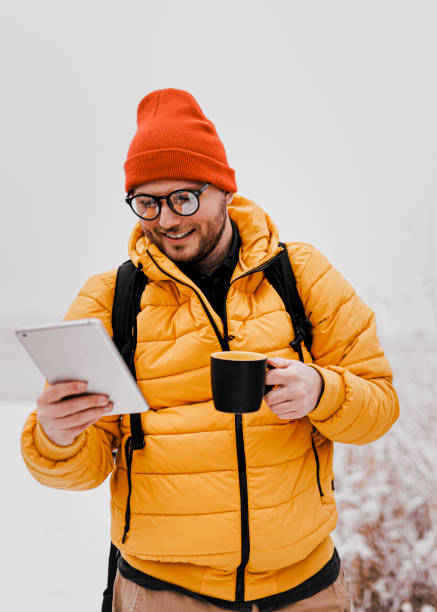 istock Man drinking hot drink and using phone in winter snowy day 1365416117