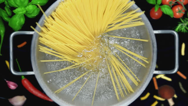 A Chef's Hand Puts Spaghetti Pasta into Pot with Boiling Water Standing on Induction Cooker - Top View