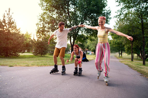 amici sorridenti che si divertono a pattinare a rotelle nel parco - pattinaggio in linea foto e immagini stock