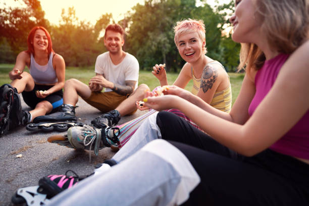 Happy young people sitting while eating popcorn together outdoors stock photo