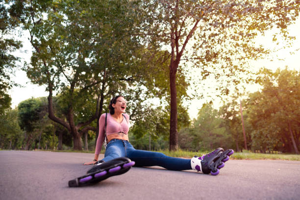 giovane pattinatrice che ride mentre è seduta sulla strada dopo la caduta - pattinaggio in linea foto e immagini stock