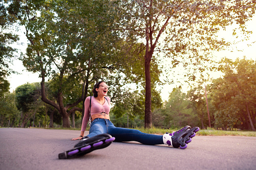 Young Caucasian woman with her roller skates on, laughing while sitting on the road after the fall.