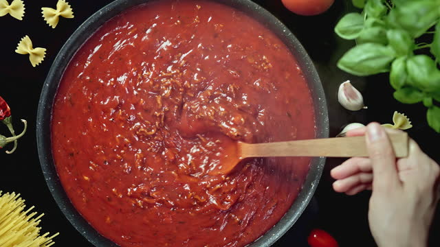 Chef's Hand Mixing Tomato Sauce with Meat Boiling in Cooking Pan on Induction Stove - Top View