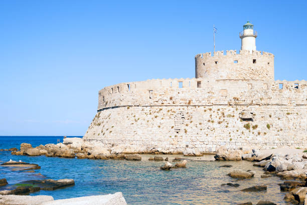 Agios Nikolaos lighthouse in Rhodes Mandraki harbour on riuns of medival fortress during sunny day against blue sky