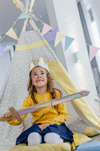 A little cute girl is inside her homemade tent, she is playing and wearing a crown
