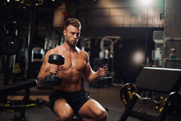 istock Determined young man lifting up dumbbells in the gym 1365427054