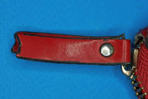 part of a wallet with a metal zip and a red leather handle on a blue background