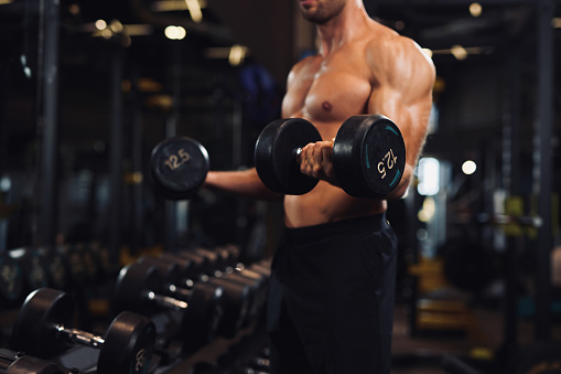 Determined young man lifting up dumbbells in the gym