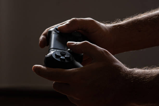 Close-up of a man's hands playing video games using a wireless controller, in a dark environment