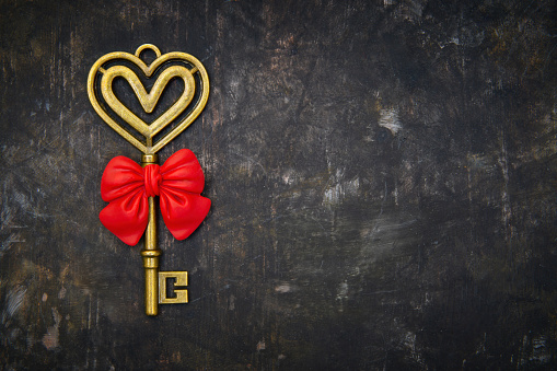 Retro style heart shaped brass key with a red bow on a grungy blackboard background with copy space. Romantic Valentine's Day present concept.