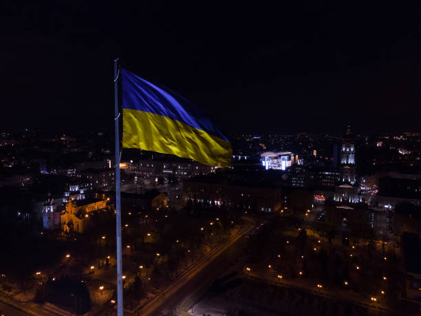 bandera ucraniana en el viento. bandera amarilla azul contra la gran ciudad por la noche - cultura de europa del este fotografías e imágenes de stock