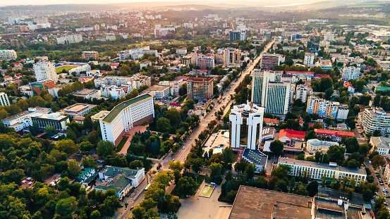 Aerial drone view of Chisinau downtown. Panorama view of multiple buildings, Parliament, Presidency, roads with moving cars and lush trees. Sunset. Moldova