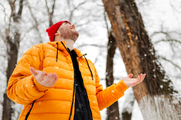 istock Cheerful man enjoying snowflakes falling from upwards 1365436354