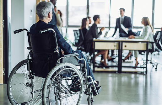 Shot of businesswoman in wheelchair at business meeting in the board room. Paralyzed woman in a wheelchair at meeting with her colleagues in the office.
