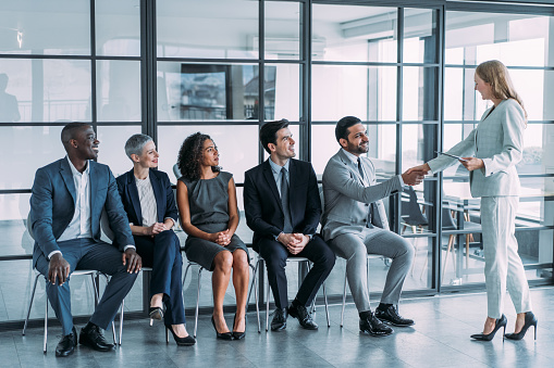 Shot of recruiter shaking hands with male job applicant. Group of business people waiting in line for job interview in modern office.