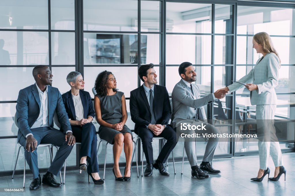HR manager handshaking with candidate at job interview. Shot of recruiter shaking hands with male job applicant. Group of business people waiting in line for job interview in modern office. Job Interview Stock Photo