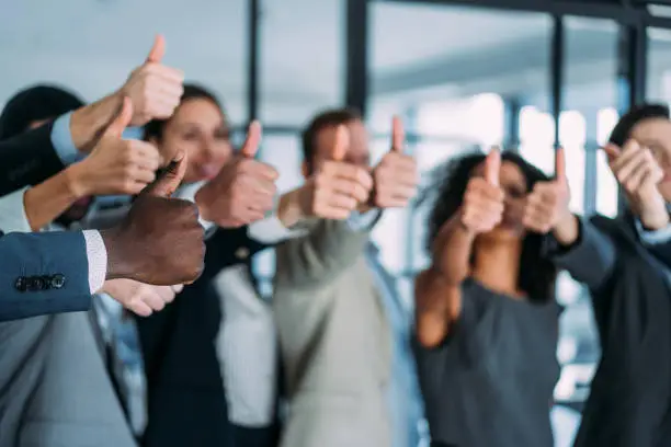 Shot of successful business team showing thumbs up sign at work. Portrait of a group of business people showing thumbs up in the office. Focus is on the thumbs.