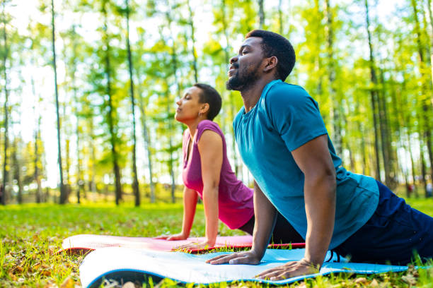 una giovane donna e un uomo attraenti che fanno yoga nella foresta verde - african descent american culture exercising women foto e immagini stock