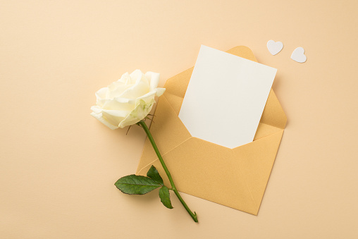 Top view photo of open pastel yellow envelope with paper sheet white hearts and white rose on isolated beige background with copyspace