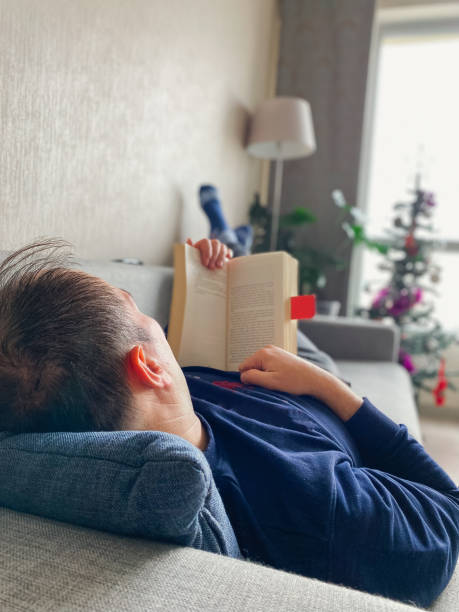 istock Man lying on couch in living room and reading a book 1365441156
