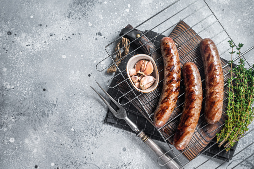 Grilled beef and lamb meat sausages with rosemary herbs on grill. Gray background. Top view. Copy space.