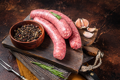 Bratwurst Raw meat sausages on wooden board with spices. Dark background. Top view.