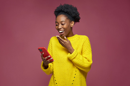 Laughing young african american woman hold phone watching funny videos in social networks mobile apps, having fun, surprised by good news. High quality photo