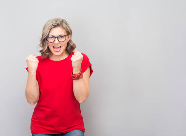 attractive middle aged woman very happy and excited doing winner gesture with arms raised, smiling and screaming for success. winner and celebration concept. - red t shirt imagens e fotografias de stock