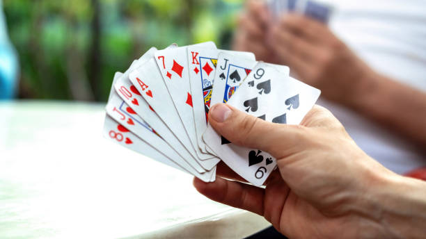 istock A man playing cards with other people holding a deck 1365443807